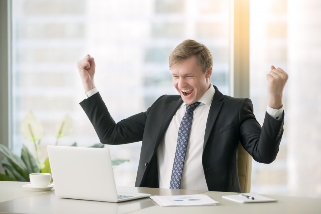 Young businessman celebrating a successful venture while looking at his laptop.