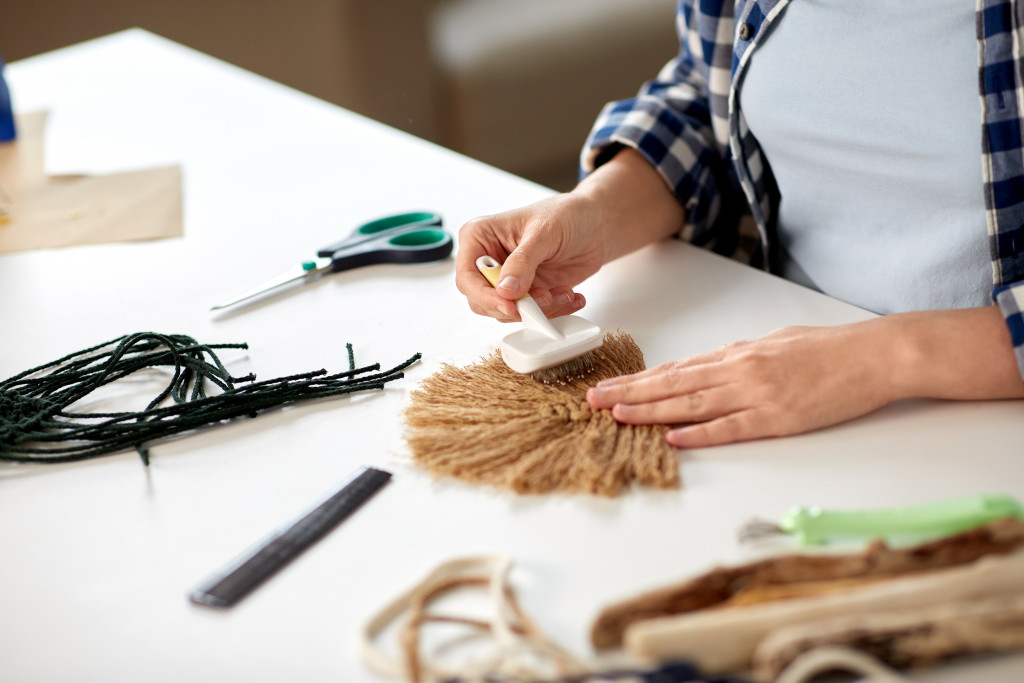 Close-up of a woman brushing Macramé item on a table at home