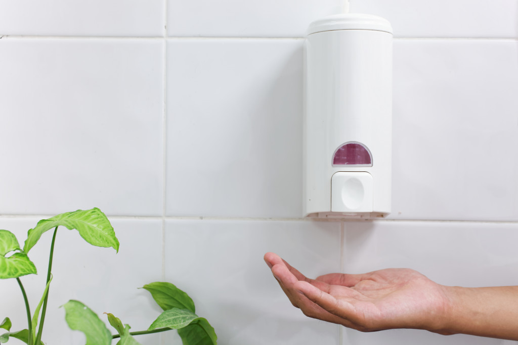 A hand under the soap dispenser in a bathroom