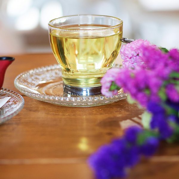 cup of green tea on a saucer, next to a red pot and flowers