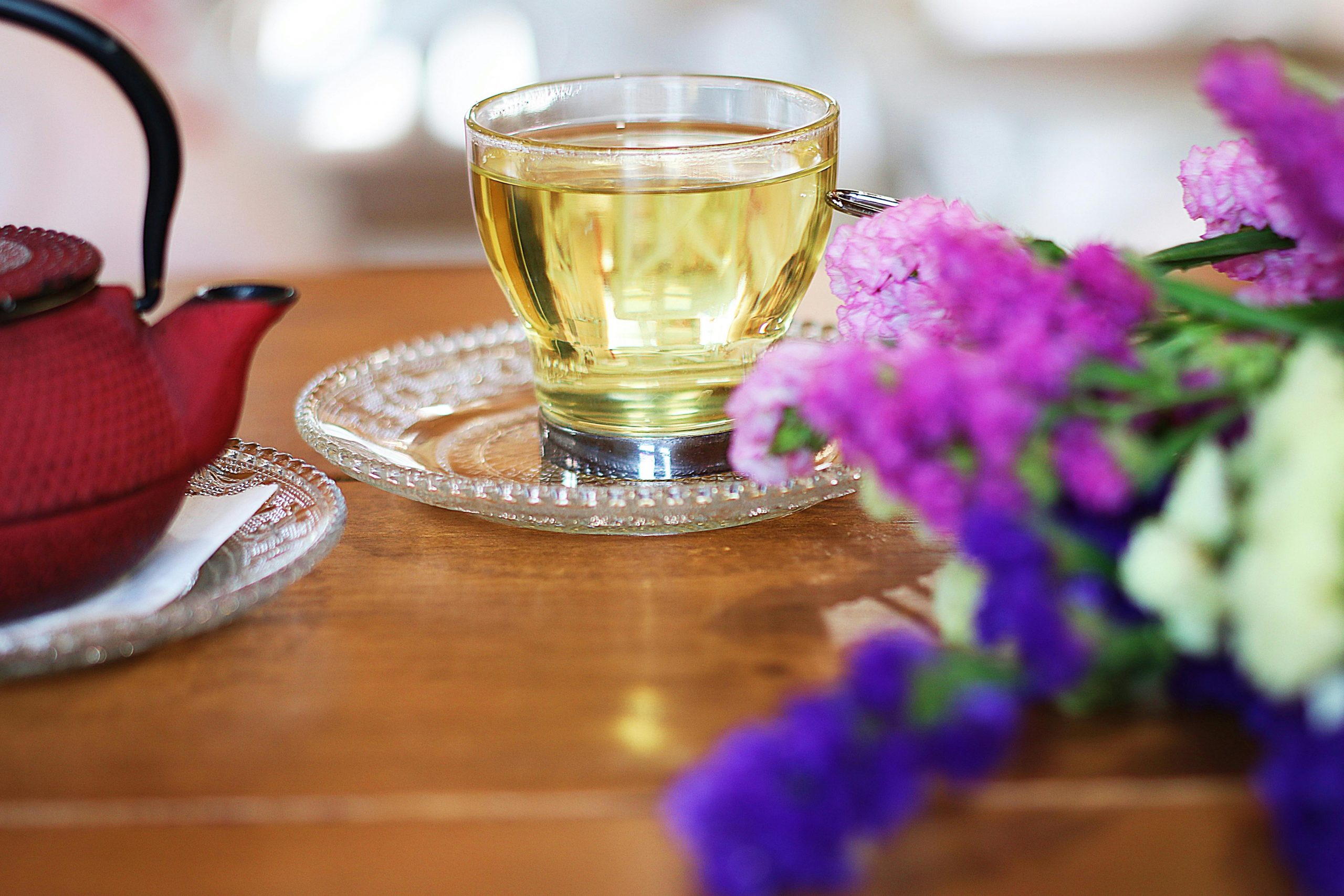 cup of green tea on a saucer, next to a red pot and flowers